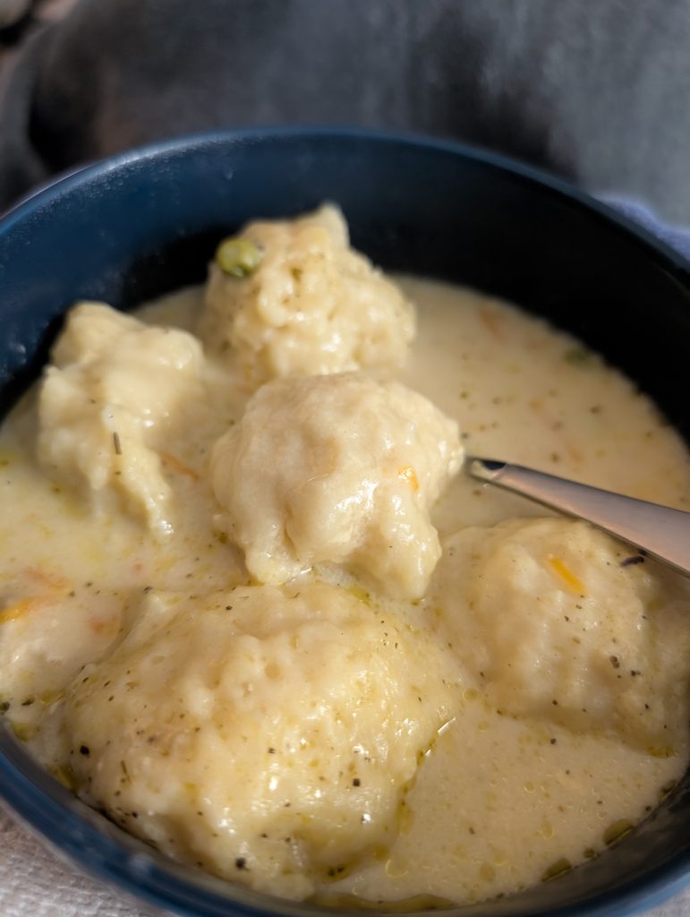 Creamy chicken and dumpling soup in a bowl with soft doughy dumplings, vegetables, and a spoon in a thick, comforting broth.