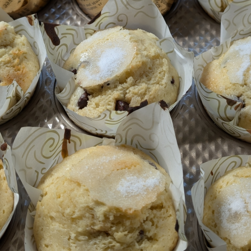 Freshly baked chocolate chip muffins in patterned paper liners arranged in a metal baking tray.