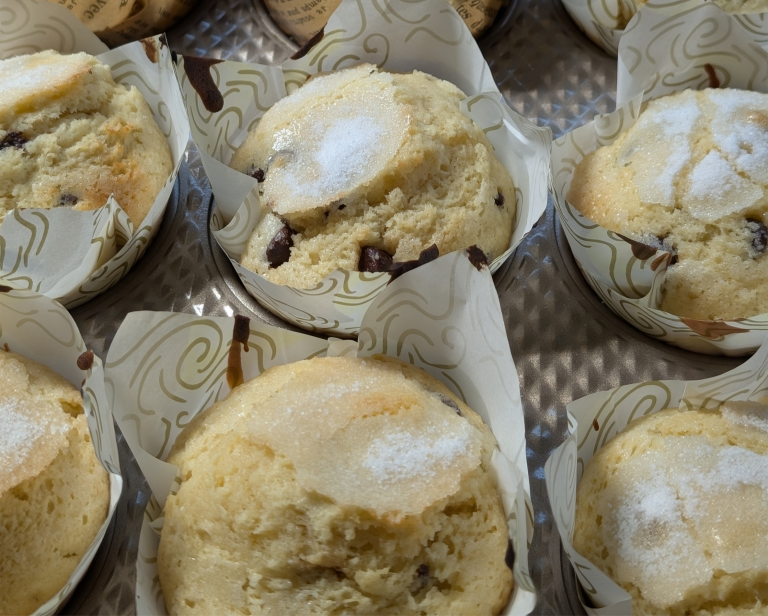 Freshly baked chocolate chip muffins in patterned paper liners arranged in a metal baking tray.