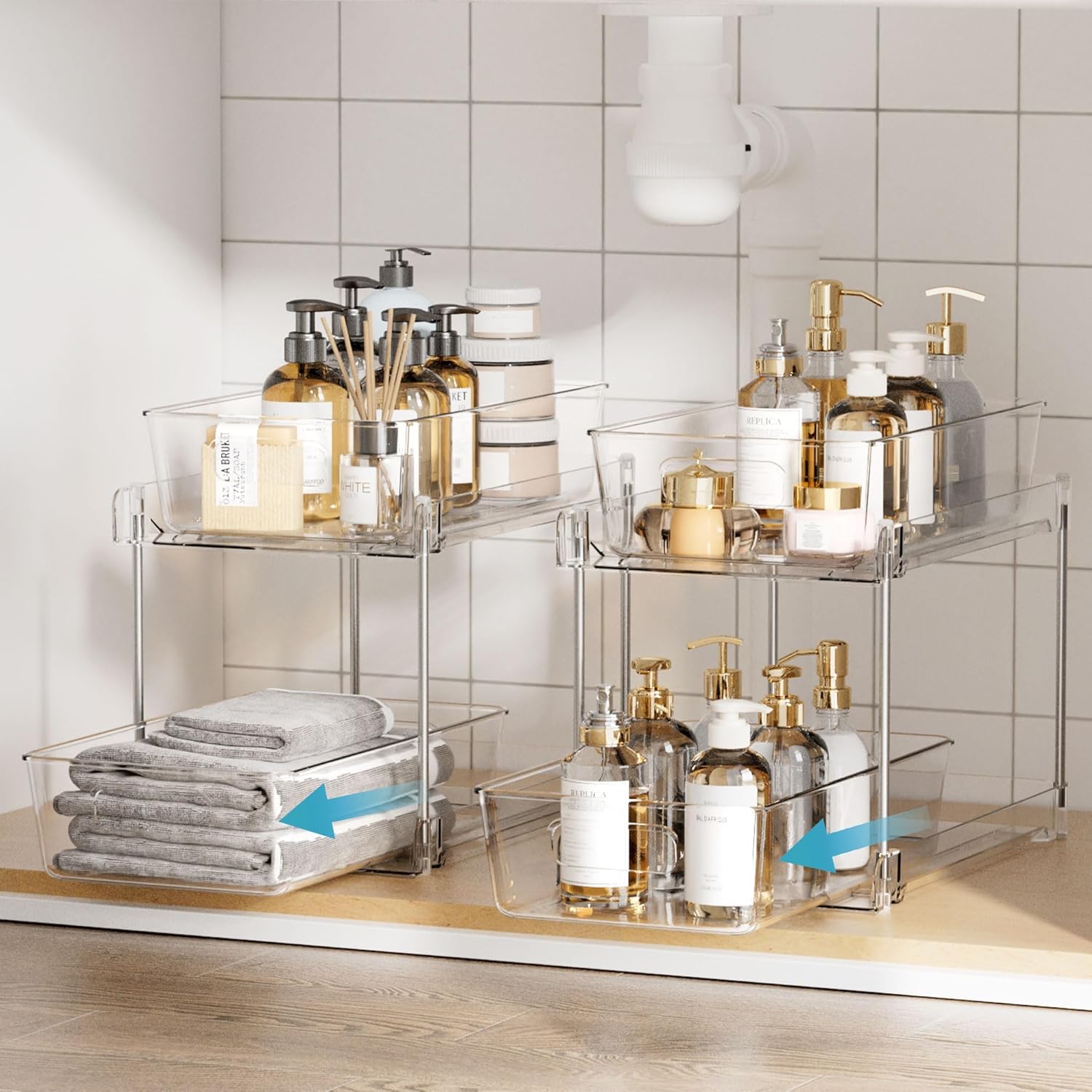 Under‑sink storage with clear pull‑out drawers holding towels, labeled bottles, and small containers in an organized bathroom or kitchen setup.