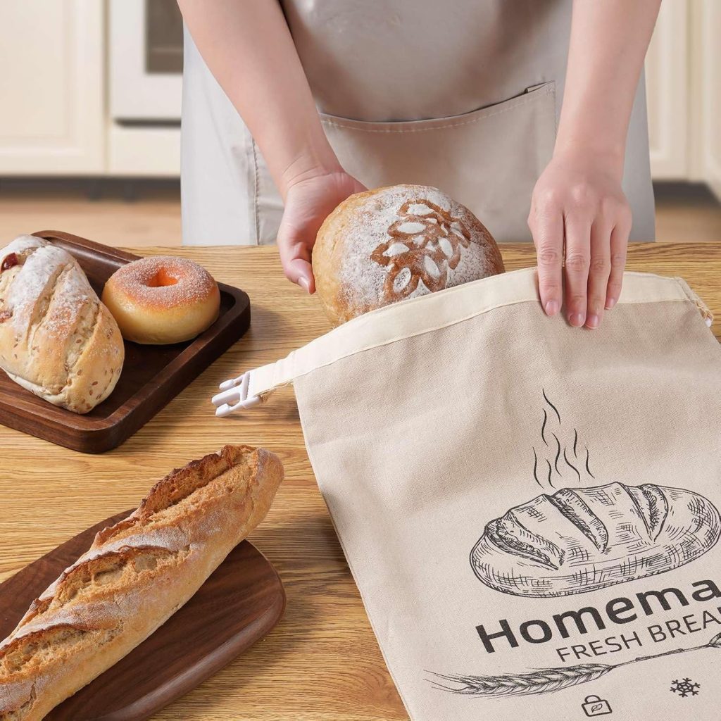Person placing a round artisan loaf into a cloth bag labeled “Homemade Fresh Bread,” surrounded by assorted baked goods on a wooden table.