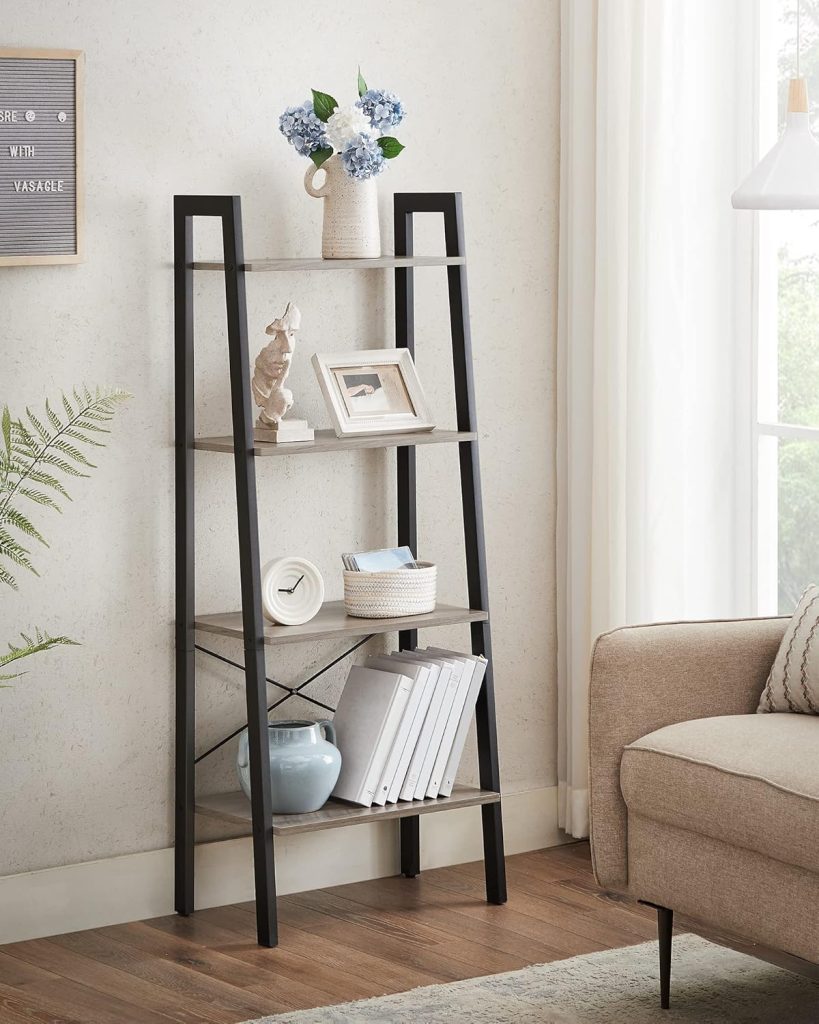 Modern ladder‑style bookshelf with wooden shelves holding hydrangeas, décor pieces, framed photo, clock, basket, and books beside a fern and upholstered chair in a bright living space.