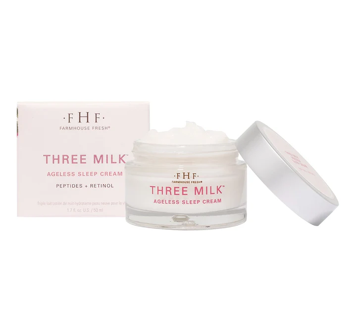 A jar of Three Milk Ageless Sleep Cream with its lid off, showing whipped white cream beside its pink product box.