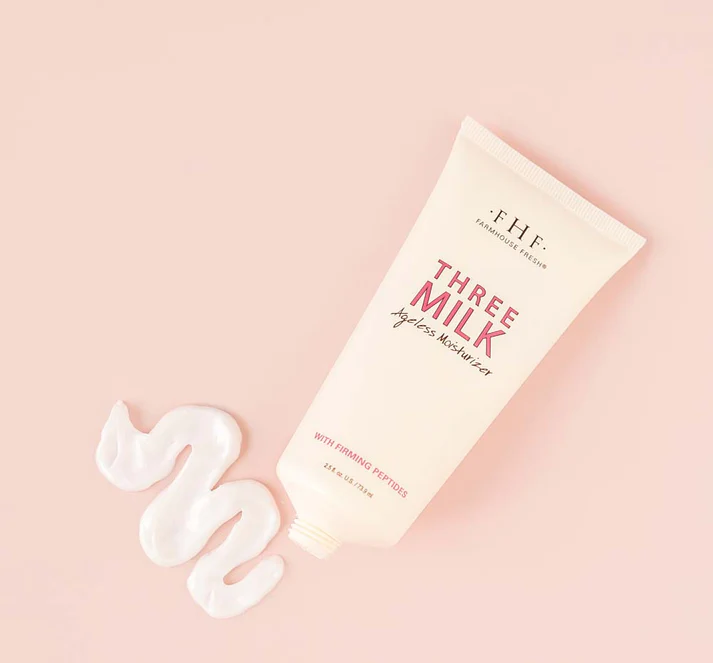A tube of Three Milk Ageless Moisturizer on a pink background with a wavy swipe of moisturizer beside it.