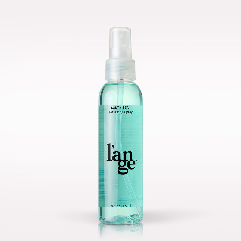 L’ange Salt + Sea Texturizing Spray in a clear 4 oz spray bottle filled with aqua-blue liquid and topped with a clear spray cap.